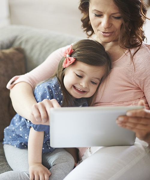 A mother and daughter sit on the couch while reviewing Just For Kids Dentistry insurance options
