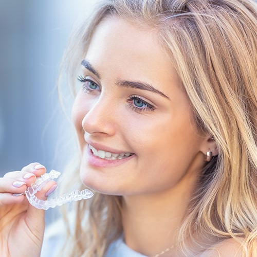A teenage girl putting on Invisalign aligners while smiling
