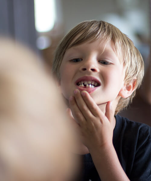 A boy looking in the mirror at his missing tooth while holding his jaw